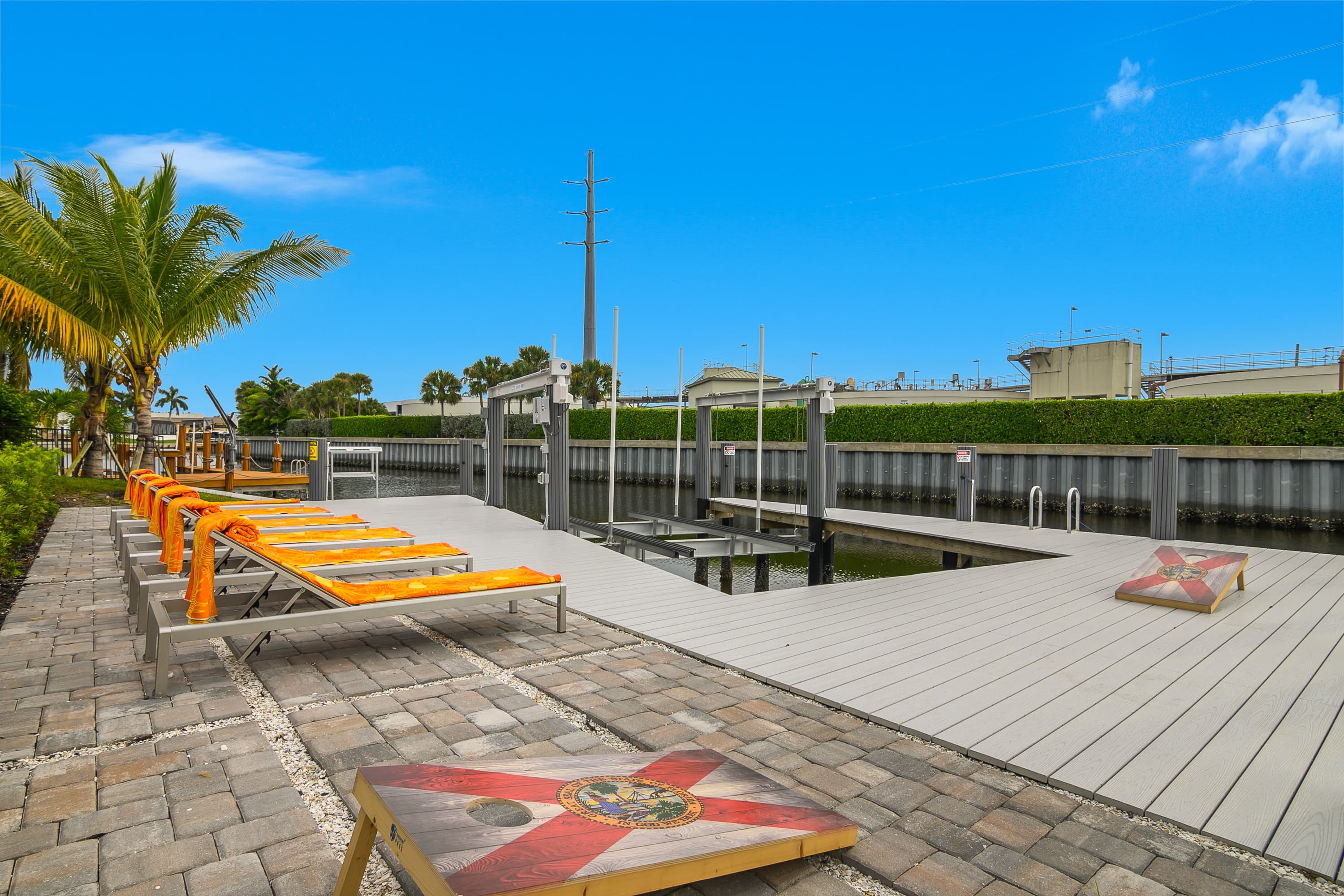 Line of orange-patterned sun loungers on paved ground near canal dock with cornhole boards