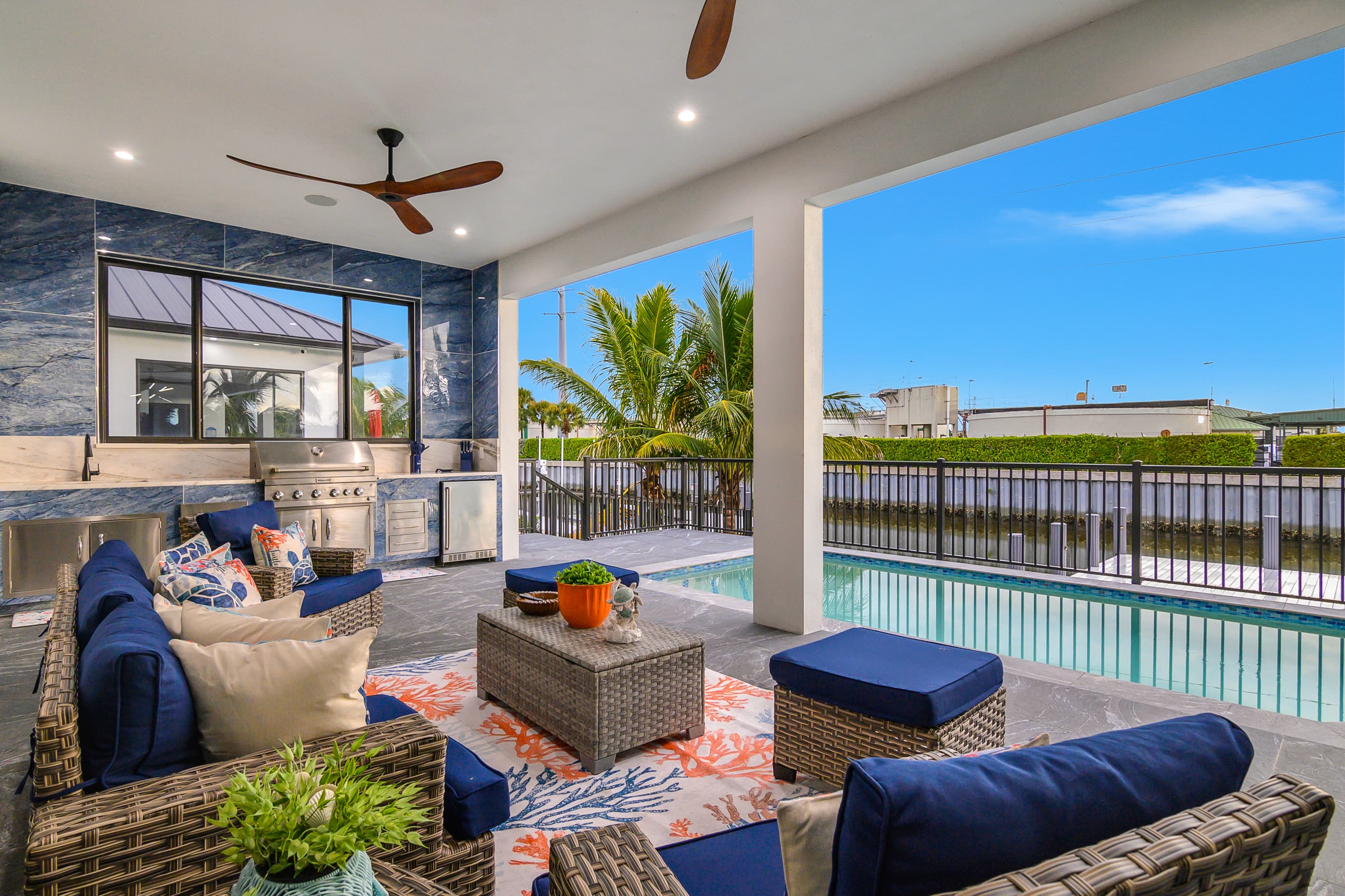 Outdoor covered lounge area with wicker furniture and navy cushions, built-in grill and small pool next to the seating area