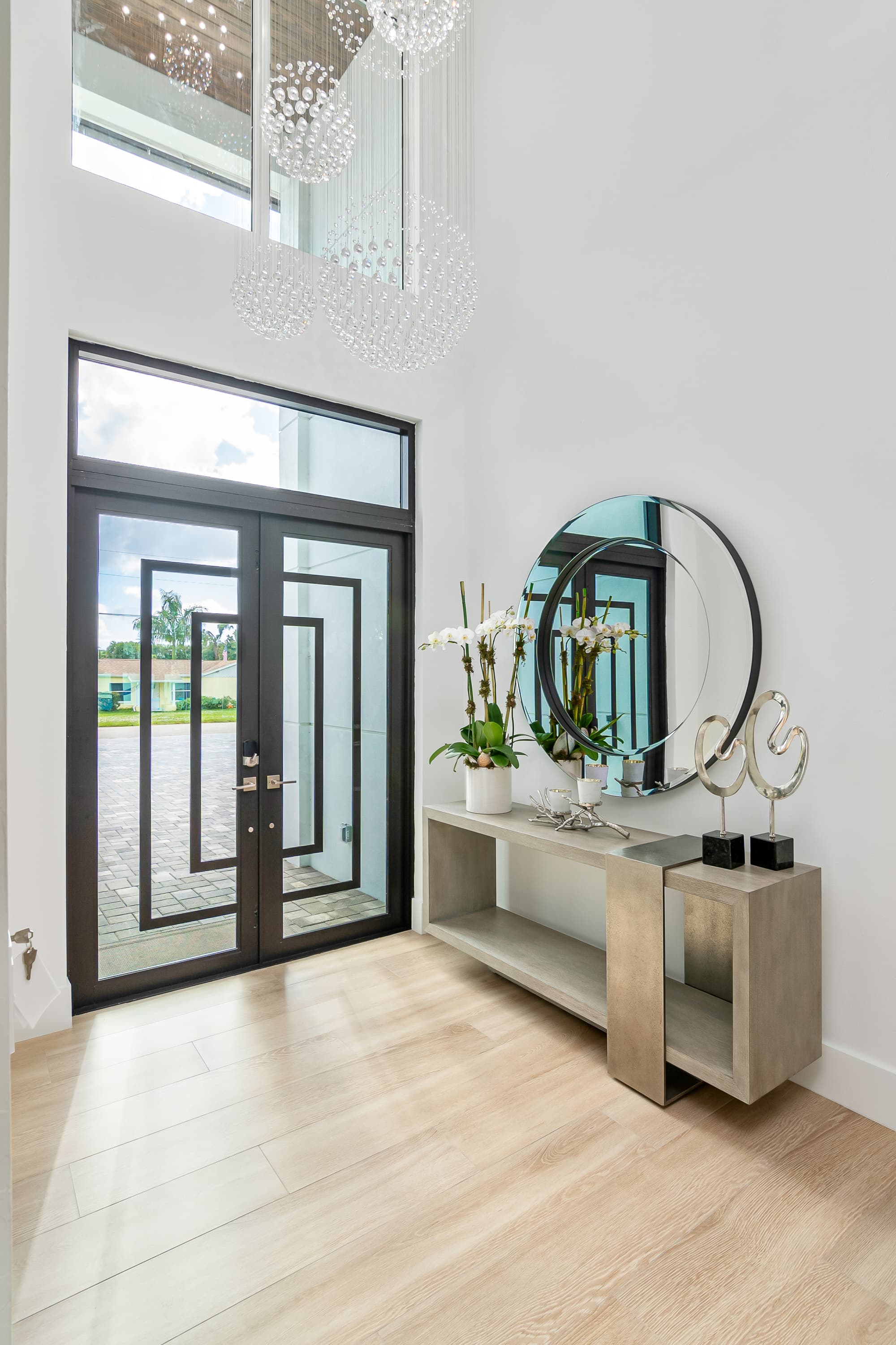 Entryway interior with a console table, round mirror and orchids near glass front door