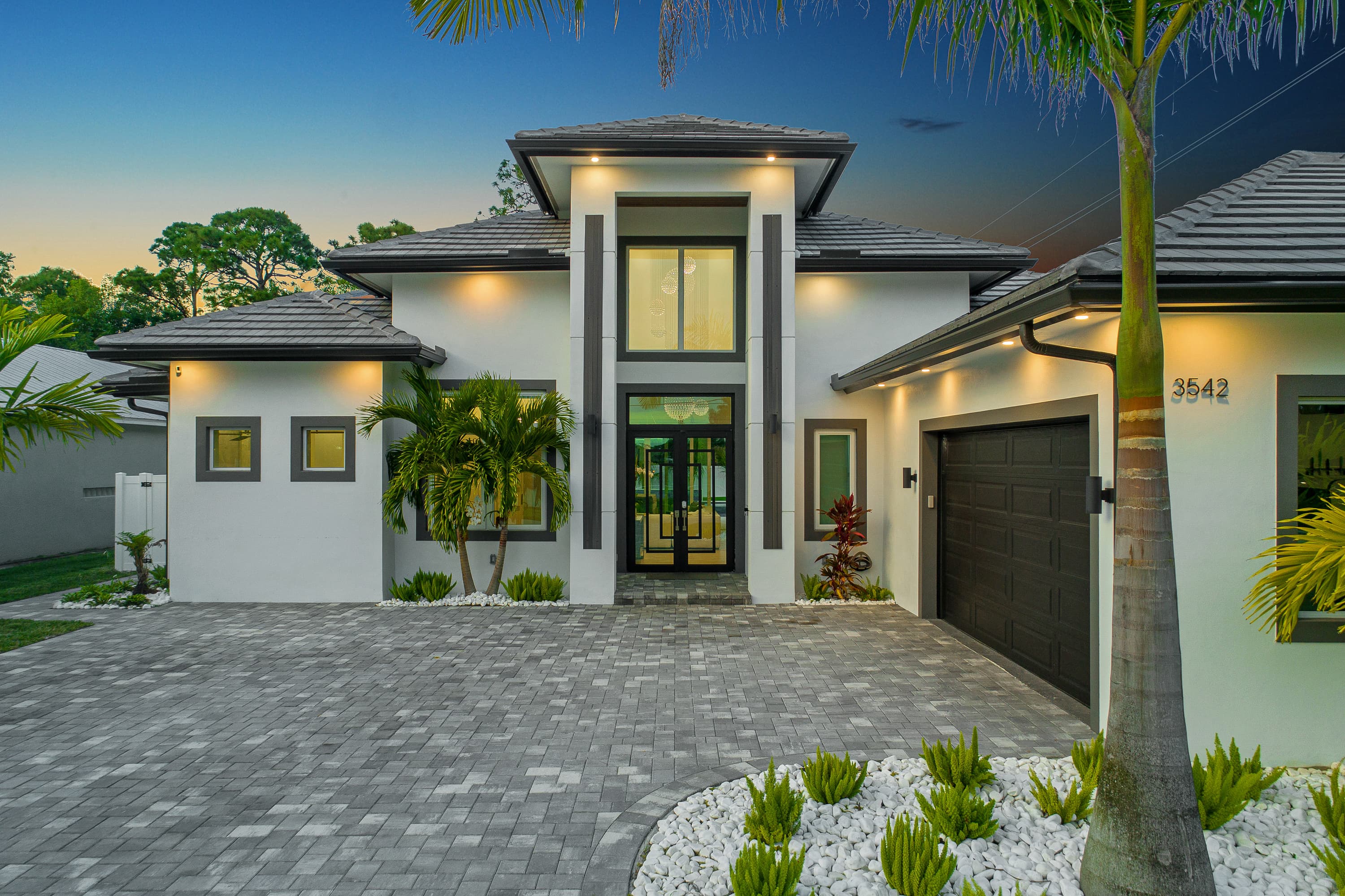 Modern exterior facade of house with front entrance, garage and landscaping at dusk