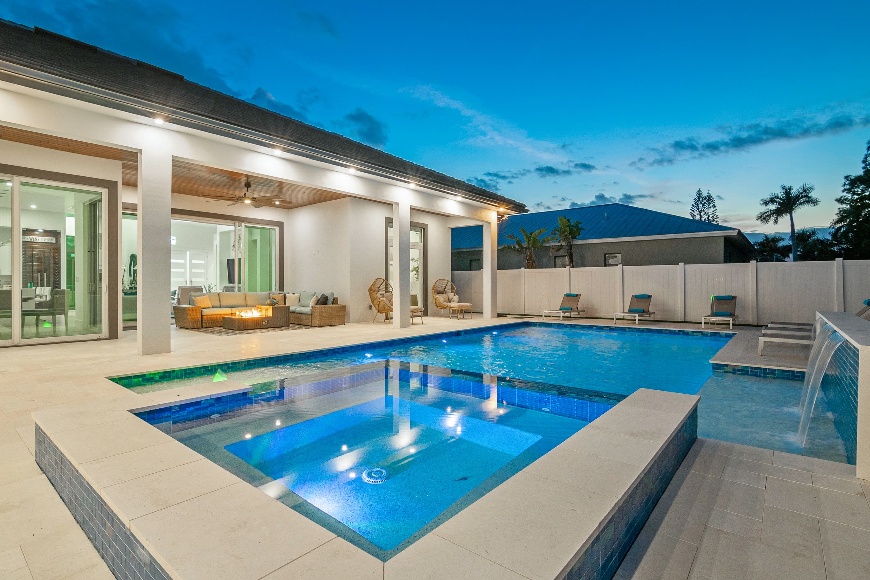 Outdoor pool and spa with integrated water features and lounge chairs under twilight sky
