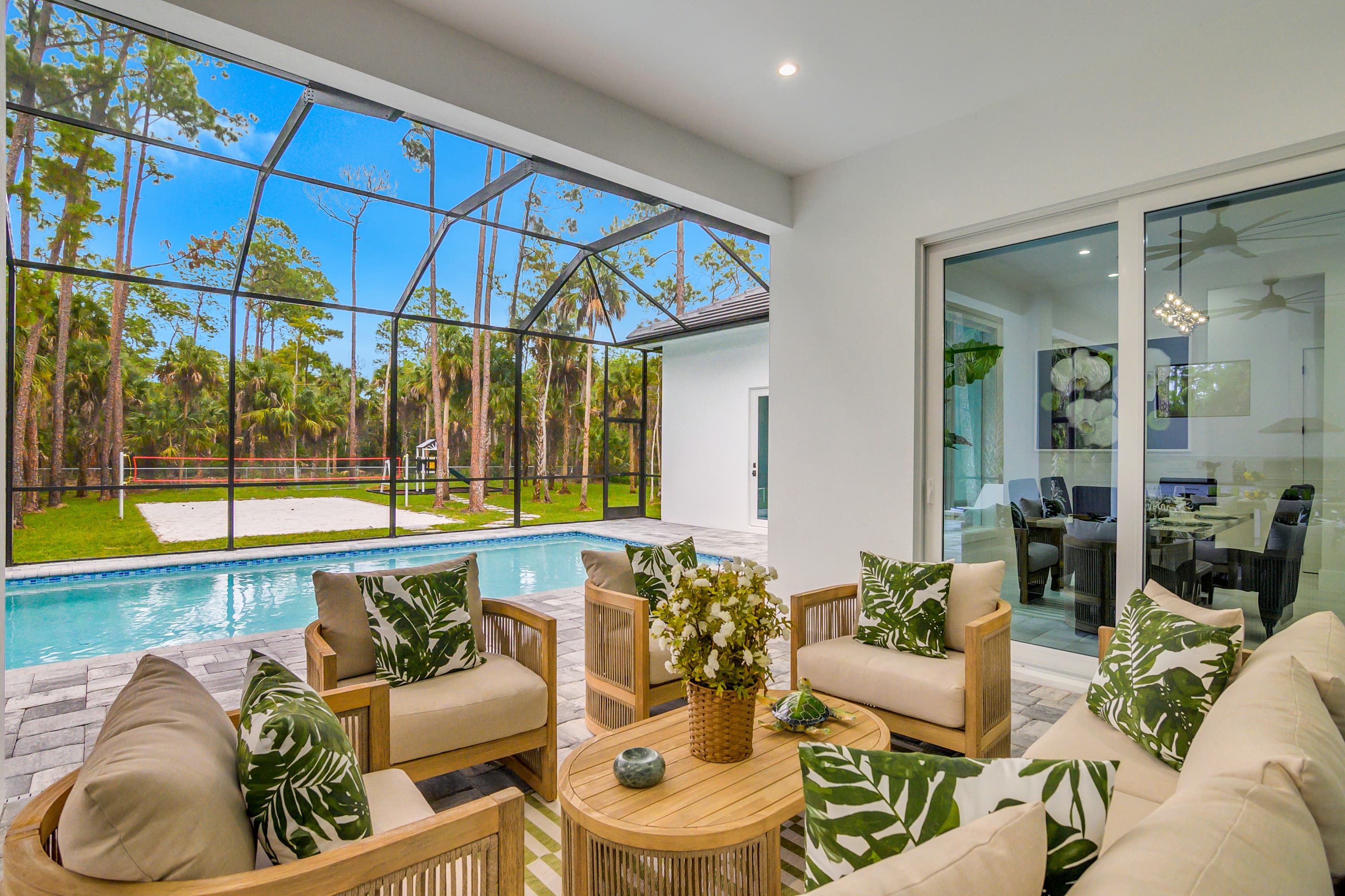 Wide nighttime view of heated pool and spa under a screened enclosure with outdoor seating and ceiling fans visible